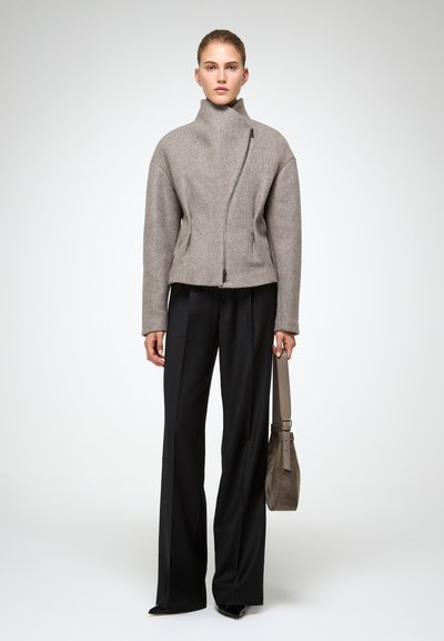 Chaqueta corta de lana gris con cuello alto y cremallera asimétrica, combinada con pantalones de pierna ancha negros y un pequeño bolso texturizado.