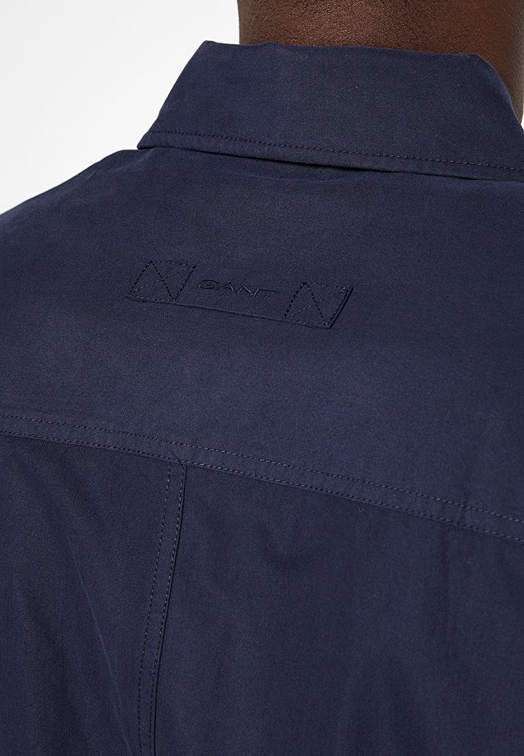 Camisa de un azul marino oscuro con un cuello simple, textura suave y un detalle de logo bordado en la parte posterior, cerca del escote.