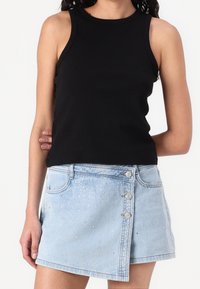 Musta ilmanhiha toppi, jossa on pyöreä pääntie, yhdistettynä vaaleansiniseen farkkuhameeseen, jossa on napit ja hopeiset niittikoristeet.