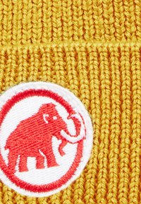 Un tissu tricoté jaune présente un patch circulaire blanc avec un dessin de mammouth rouge, mettant en valeur la texture et le contraste vif des couleurs.