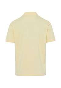 Polo shirt in soft yellow cotton, short sleeves, classic collar, clean lines, and minimal stitching without any visible branding.
