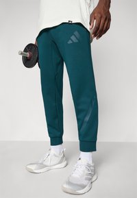 Tegneblå sweats med en tapered design, der har en diskret blank stribe og et adidas-logo. Sammen med grå træningssko og hvide sokker.