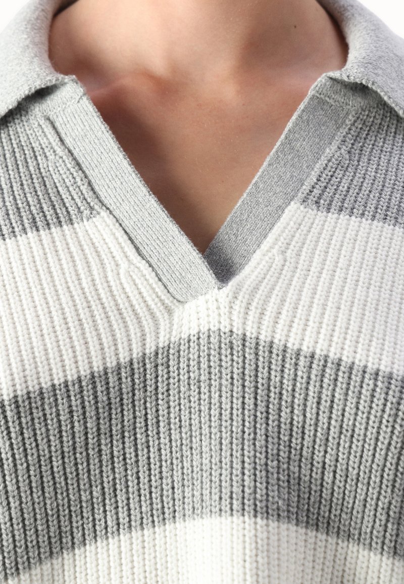 Szary i biały sweter z prążkowanego materiału, z dekoltem w kształcie litery V i kołnierzykiem. Tekstura jest prążkowana, z pasami w kontrastowych kolorach.