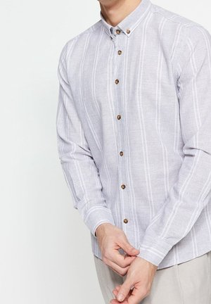 Man wearing light gray button-up shirt with white vertical stripes fastening cuff, shown from neck to hips against white background.