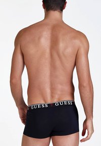 Fekete pamut boxer alsónadrág fehér derékkal, amin a "GUESS" logó látható. A modell háta és válla látható, további részletek nélkül.