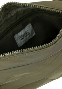 Grøn lynlåspose med et glat, struktureret stofinteriør. Har en sølv lynlås og en label indeni. Dyb og rummelig design.