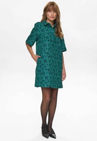 Rochie cu imprimeu de frunze verzi, cu mâneci scurte, guler, două buzunare laterale și croi drept. Purtată cu ciorapi negri și pantofi cu vârf ascuțit.