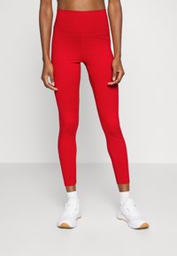 Leggings rossi a vita alta con un design aderente, texture liscia e materiale elastico. Abbinati a scarpe da ginnastica bianche.