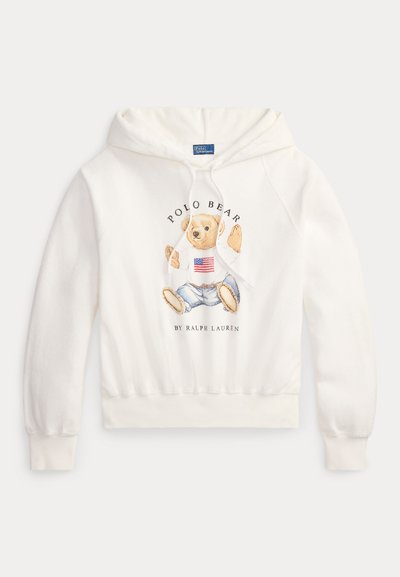 Hanorac alb cu un urs purtând un pulover cu steagul american și blugi, textul "Polo Bear by Ralph Lauren" pe față.