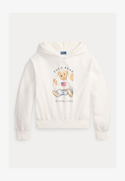 Hanorac alb cu un urs purtând un pulover cu steagul american și blugi, textul "Polo Bear by Ralph Lauren" pe față.