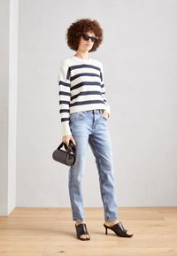 Striped knit sweater in navy and white, light blue denim jeans, black open-toe mules, and a textured black handbag.