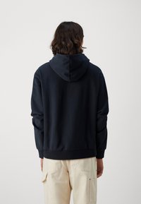 Sudadera con capucha azul marino, con un ajuste relajado, puños y dobladillo acanalados, fabricada con tela suave y un diseño sencillo y minimalista.