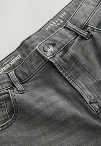Mørkegrå denimjeans med barrel-fit design, lukkes med metalen knap, og hvid branding på linningen. Simpelt design med fem lommer.
