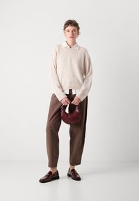 Lys beige ullgenser, brune løstsittende bukser, skinnende burgunder loafers og en strukturert burgunder håndveske med buet håndtak.