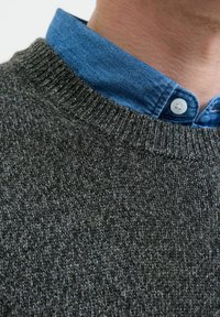 Pull en tricot gris foncé avec un col côtelé, superposé sur une chemise à col bleu clair avec des boutons.