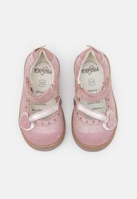 Para różowych bucików Mary Jane dla małych dzieci z paskami w kształcie serca i brązowymi gumowymi podeszwami, pokazana z góry na białym tle.