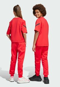 Röd idrottsset med kortärmad topp och smala byxor. Slätt tyg med svarta detaljer på ärmarna. Vita och svarta sneakers.