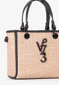 Borsa a tracolla beige in tessuto intrecciato con manici in pelle nera, bordi neri e un ciondolo con logo "v73" in metallo nero attaccato vicino al bordo superiore.