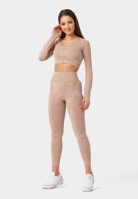 Lichtbruine sportoutfit bestaande uit een cropped langemouwen top en hoge taille legging, gemaakt van tekstiel met een logo detail.