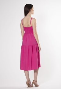 Fuchsia midi-jurk met spaghettibandjes, smocktop en gelaagde rok. De stof is lichtgewicht met een soepele textuur.
