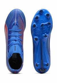 Scarpe da calcio blu con accenti rossi e neri, lacci sopra e suole chiodate, mostrate dalla vista superiore e inferiore.
