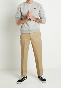 Šedá mikina s kulatým výstřihem, khaki kalhoty, černé tenisky. Bavlněný materiál, žebrované manžety a lem, logo na prsou. Přiléhavý střih.