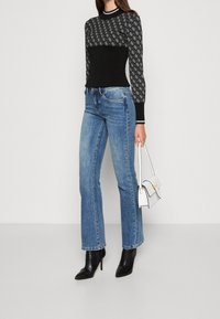 Top nero a maniche lunghe con maniche a motivo, abbinato a jeans svasati azzurri chiari. Accessoriato con una piccola borsa bianca e stivali neri con tacco.