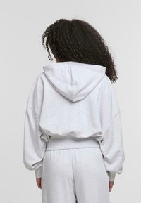 Felpa oversized grigio chiaro con cappuccio, spalle cadute e polsini a costine. Tessuto morbido con una finitura leggermente testurizzata.