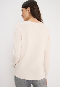 Lichtbeige langemouwen T-shirt met een ronde hals, zachte textuur en een licht gebogen zoom. Kenmerken zijn onder andere een casual pasvorm en minimale naden.
