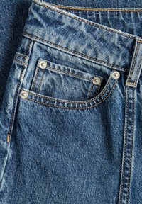 Denim tkanina u svijetlop plavoj nijansi sa suptilnim izbljedeleljem. Uključuje mali prednji dzep i kontrastne smeđe šavove.