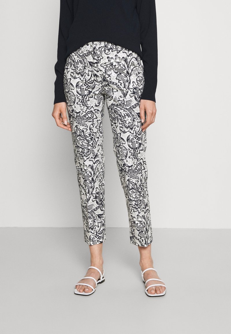 Zwart-witte gestreepte broek met een bloemenpatroon, tapered fit en elastische tailleband, gecombineerd met witte sandaaltjes met banden.