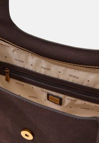 Borsa in tessuto marrone con tasca interna con zip, fodera beige con motivo ripetuto "GUESS" e dettagli in metallo dorato.