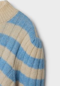 Nahaufnahme der Schulter eines gestrickten blau-beigen gestreiften Pullis mit gerippter Textur und Puffärmel-Detail.