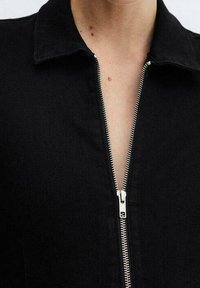 Černý zip-up top s límečkem, s stříbrným zipem, hladkou strukturou a přiléhavým střihem. Bez dalšího zdobení nebo vzorů.