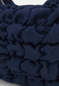 Gros plan sur un tissu bleu foncé froncé avec des volants denses et un détail de tissage texturé visible.