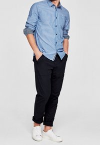 Blauw-wit gestreepte overhemden met lange mouwen, gecombineerd met zwarte broeken en witte sneakers. Het overhemd heeft een borstzak en opgerolde mouwen.