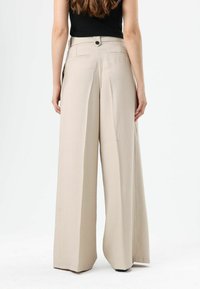 Beige wijde broek met hoge taille, voorzien van een knoopsluiting en twee achterzakken, gemaakt van een gladde stof.