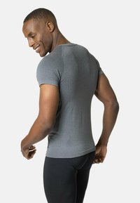 Camiseta atlética gris de manga corta con un patrón texturizado, diseño ajustado y tejido suave, combinada con pantalones deportivos negros.