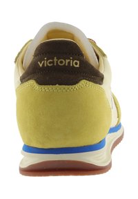 Tacco di sneakers in suede giallo con colletto marrone, interno bianco, striscia blu sulla suola intermedia e scritta "victoria" sul retro del colletto.