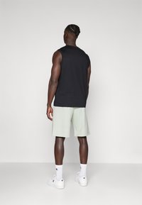 Black sleeveless tank top, light green shorts, white sneakers. Simple design, cotton material, relaxed fit, and knee-length shorts.