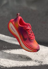 Nike ZoomX trkačka cipela u živopisnoj ružičastoj i narančastoj gradaciji, sa teksturiranom mrežastom gornjom fudbalericom, obućenom sole s jastučićima i crnim swoosh logom.