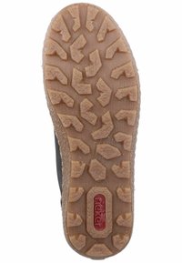 Semelle extérieure en caoutchouc avec une surface texturée présentant un motif de bande de roulement multidirectionnel. La couleur est marron clair avec un logo rouge et blanc.
