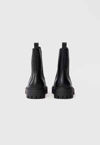 Botas de tobillo de cuero negro con suela gruesa texturizada y una lengüeta en la parte posterior. Diseño elegante con detalles mínimos.