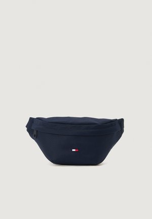 Sac banane bleu marine en tissu durable avec fermeture éclair. Présente un petit logo rouge, blanc et bleu. Forme compacte et arrondie.
