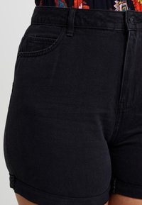 Shorts de mezclilla negra de tiro alto, con un bolsillo frontal, dobladillo enrollado y una textura suave. Detalle de costura visible.