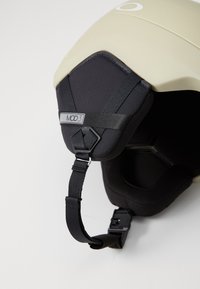  casco de nieve en beige con acabado mate y acolchado negro. Cuenta con un sistema de correas ajustables y un forro interior hexagonal para mayor comodidad.