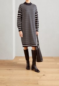 Mustavalkoraidallinen neulemekko pitkillä hihoilla, pyöreällä kaula-aukolla ja sivuhalkioilla, yhdistettynä polven yli ulottuviin mustiin nahkabootseihin ja laukkuun.