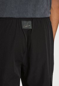 Svarta sportiga byxor med en slät textur och elastisk midjeresår, utrustade med en läderetikett med präglad logotyp framtill.