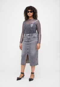 Top trasparente a maniche lunghe con stampa animalier, gonna in denim grigia con spacco frontale e tacchi neri con cinturini e dettagli metallici.