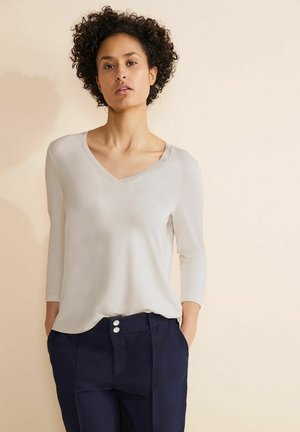 Maglietta a maniche lunghe beige chiaro con scollatura a V, realizzata in tessuto morbido. Abbinate a pantaloni blu navy con due bottoni bianchi.